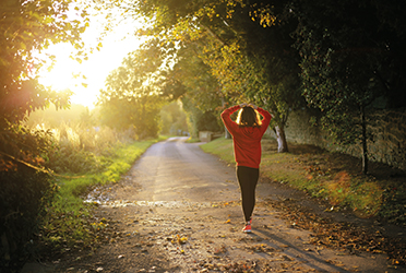 Das Bild zeigt eine Frau in Sportkleidung, die auf einem Weg durch einen Wald geht. (verweist auf: Dialog­forum Nach­haltiger Sport mit BISp-Beteili­gung)