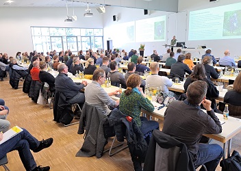Das Foto zeigt einen veranstaltungsraum, in dem eine große Gruppe Menschen einen Redner auf dem Podium zuhören (verweist auf: 6. Osnabrücker Sportplatz­tage: urbane Sport­freianlagen betreiben)